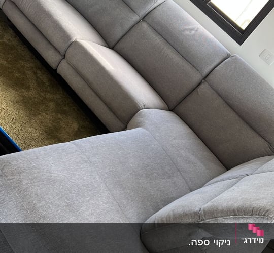 ספה אפורה גדולה ליד חלון עם אור שמש